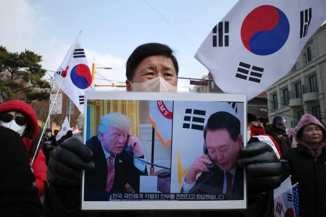 A supporter of impeached South Korean president Yoon Suk Yeol holds a placard of Yoon (R) and incoming US president Donald Trump (L) that translates as “He responded by sending his special regards to the people of South Korea”, during a rally near his residence in Seoul on January 6, 2025. South Korean investigators trying to arrest suspended President Yoon Suk Yeol have asked for an extension to the warrant that expires on January 6, with the embattled leader holed up in his residence. (Photo by Anthony WALLACE / AFP)