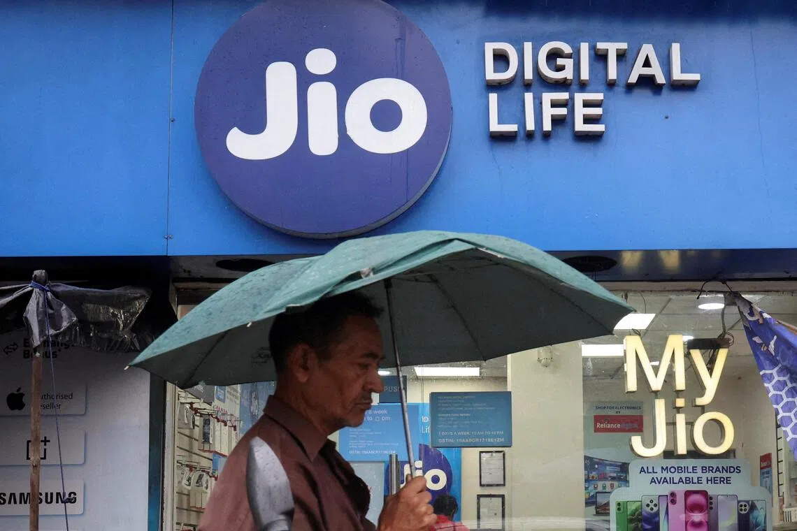 A man walks with an umbrella in front of a Reliance Industries’ Jio Digital Life store on a street in Kolkata, India, on June 19.