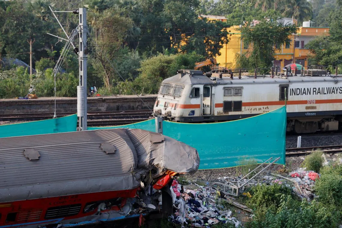 A train moves past a damaged coach after railway services were restored near the collision site in Odisha, India, on June 5.