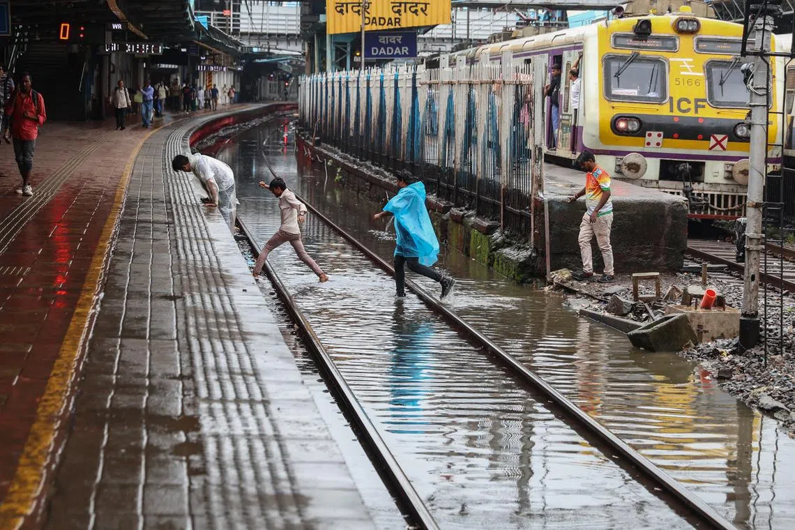 People cross flooded railway tracks during heavy rain in Mumbai on Aug 16.
