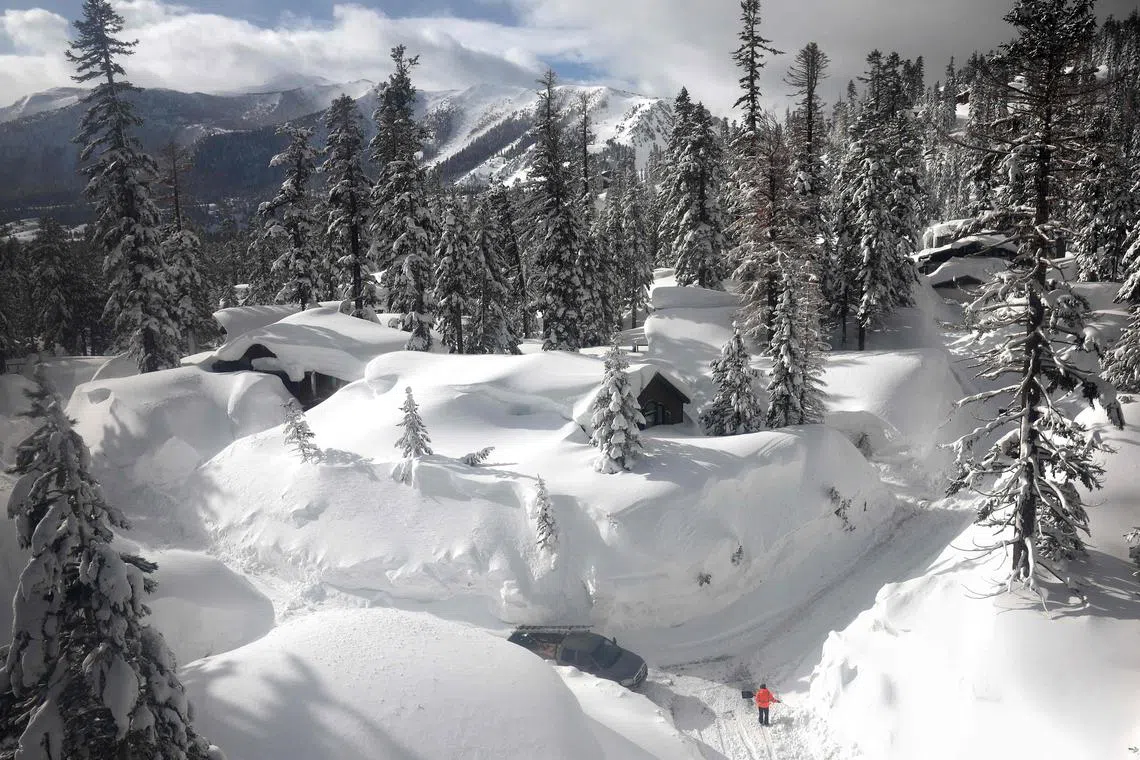 In an aerial view, a person in Mammoth Lakes shovels on a snowy roadway lined with snowbanks piled up from new and past storms in the Sierra Nevada mountains on March 12, 2023. 