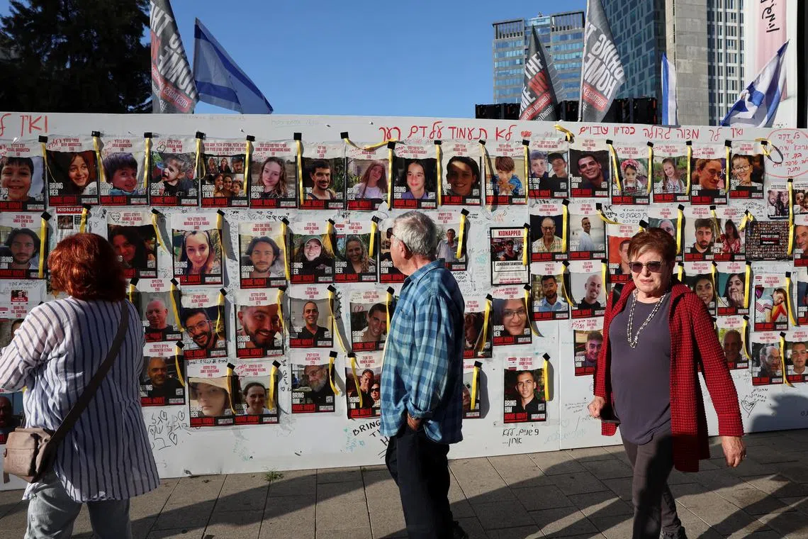 People walk past a wall in Israel's Tel Aviv, featuring posters of missing people.