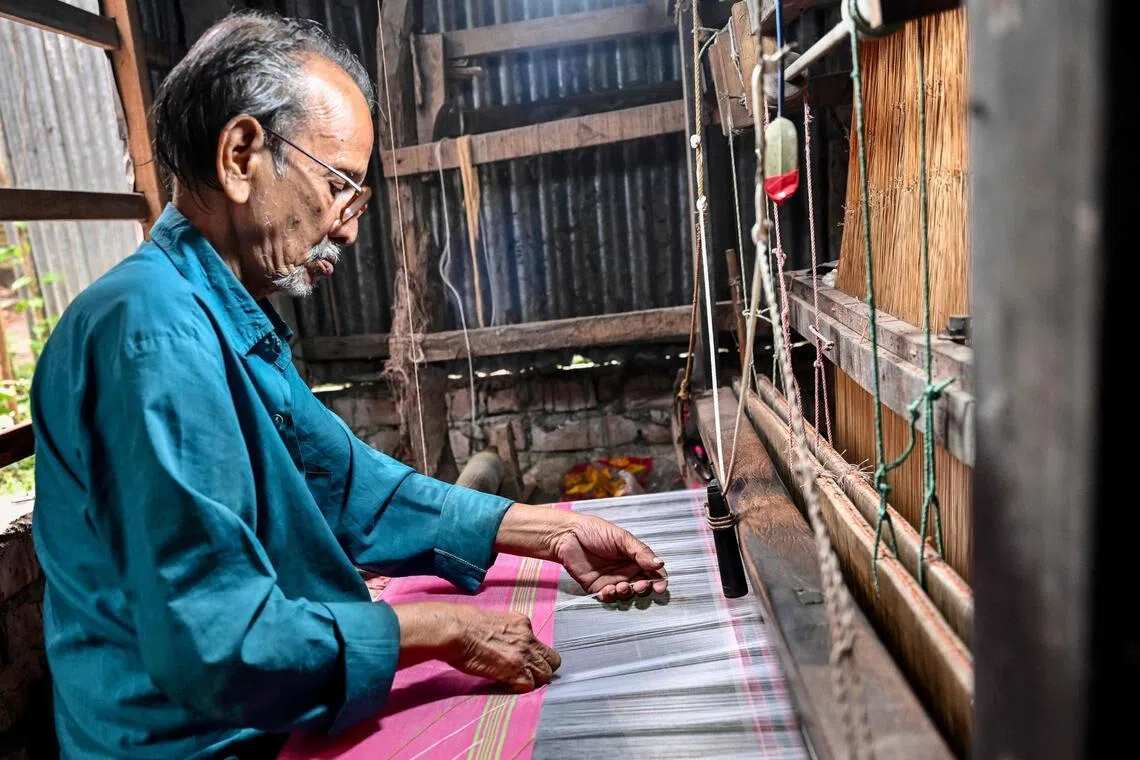A Bangladeshi craftsman weaves fabric on a traditional handloom inside a workshop in Tangail on March 2, 2026. Bangladesh's Tangail sari is fighting for survival as weavers warn that automation and economic pressures are pushing the centuries-old craft to the brink despite its global acclaim. (Photo by Munir UZ ZAMAN / AFP) / To go with 'Bangladesh-Culture-Textile', FOCUS