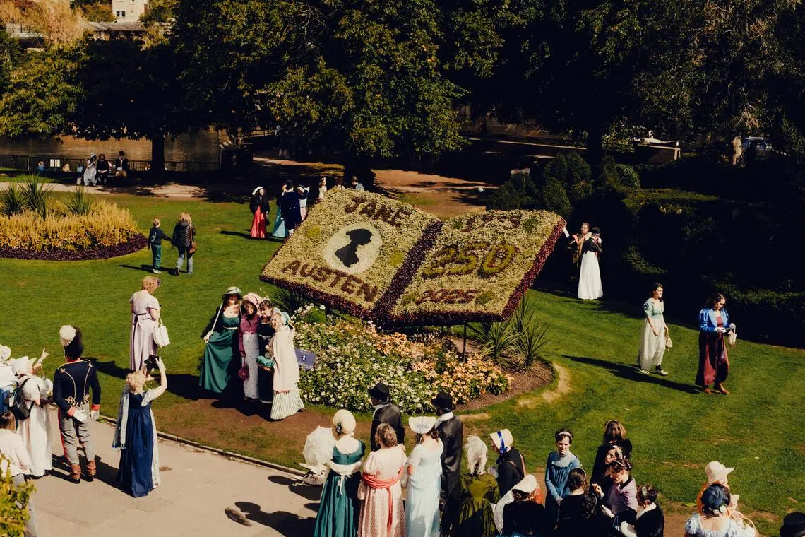 FILE — Costumed attendees take photos with a large flower arrangement during the Grand Regency Costumed Promenade at the annual Jane Austen Festival in Bath, England, on Sept. 12,  2025. To capture the writer’s brief life and enormous impact, we assembled a sampling of the wealth, wonder and weirdness she has brought to our lives. (Peter Flude/The New York Times)