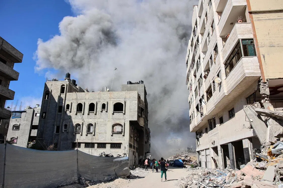 TOPSHOT - Palestinians watch as smoke rises from a building hit by an Israeli strike after a warning from the army to its occupants to evacuate the premises, in the Rimal neighbourhood of central Gaza City on August 21, 2024, amid the ongoing conflict between Israel and the militant Hamas movement. (Photo by Omar AL-QATTAA / AFP)