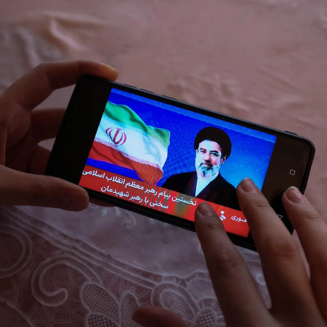 A girl watches a televised statement by Iran's new supreme leader, Ayatollah Mojtaba Khamenei, on a mobile phone. His remarks were read out by a state TV presenter.