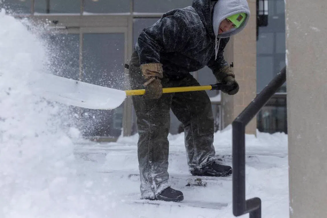 A worker removes snow from the sidewalk after a blizzard left several inches of snow in Ankeny, Iowa, U.S., January 12, 2024. REUTERS/Alyssa Pointer