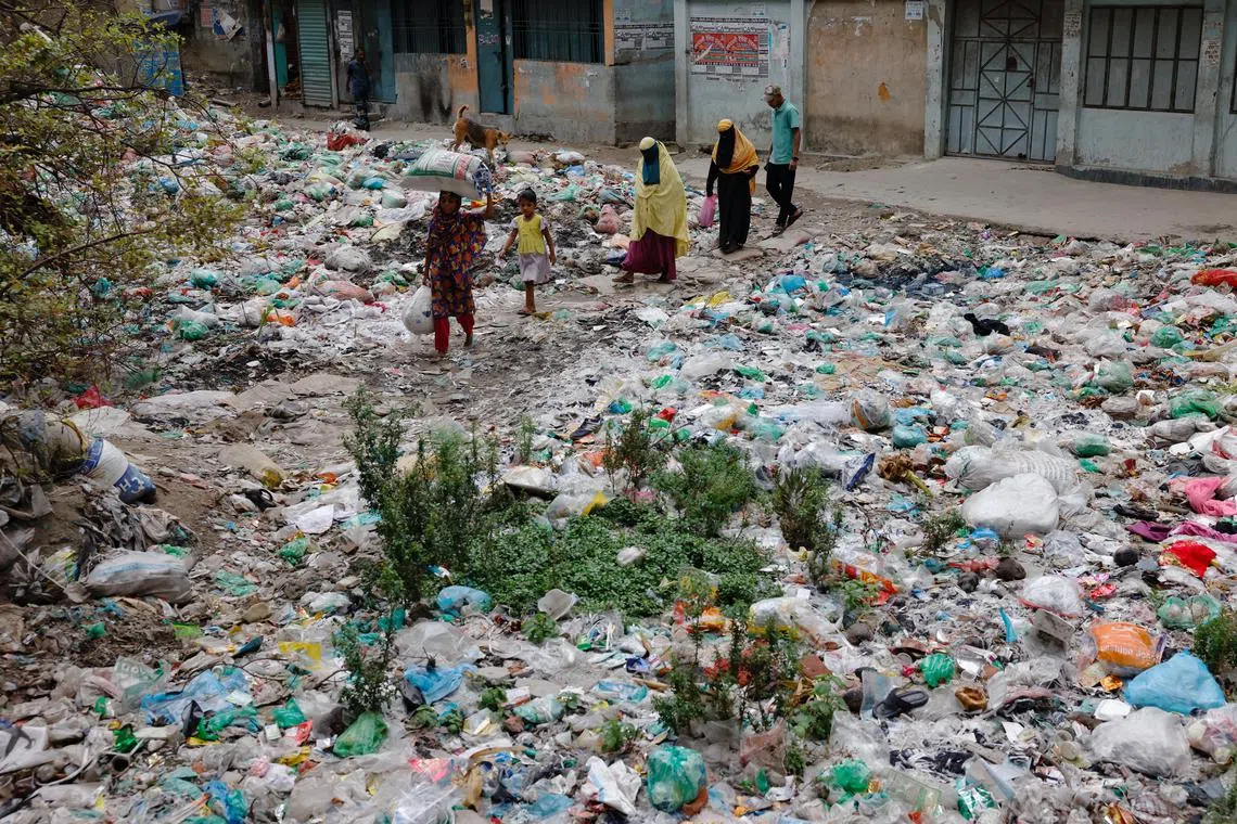 People in Bangladesh's capital, Dhaka, crossing a canal which is under a pile of plastic waste.
