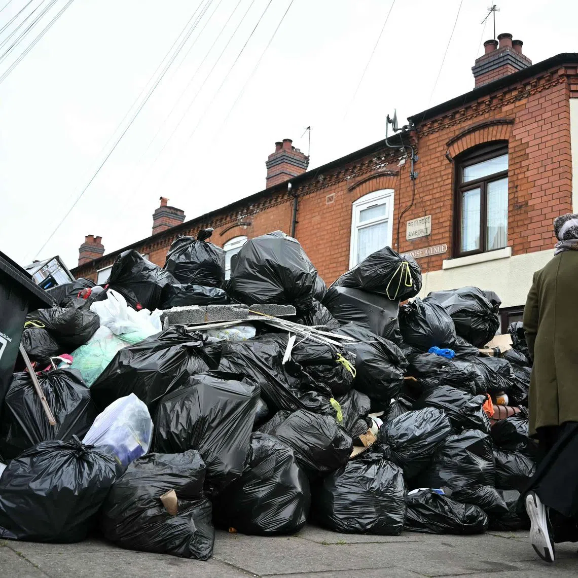 A resident walks past uncollected bin bags piled up on Poplar Road in Birmingham, central England, on April 15, 2025. Residents are desperately trying to get rid of an estimated 17,000 tonnes of trash that has piled up since refuse workers ramped up a strike last month. Four weeks in, the city council has declared a "major incident," the prime minister has had to defend the government's response in parliament, and residents say their problems are worsening by the day. (Photo by Paul ELLIS / AFP)