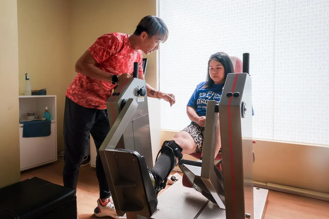 ActiveSG Instructor Victor Ng, 51, helps stroke survivor Maya Seah, 44, as she works on strengthening her legs at the Enabling Village ActiveSG Gym on Dec 19.