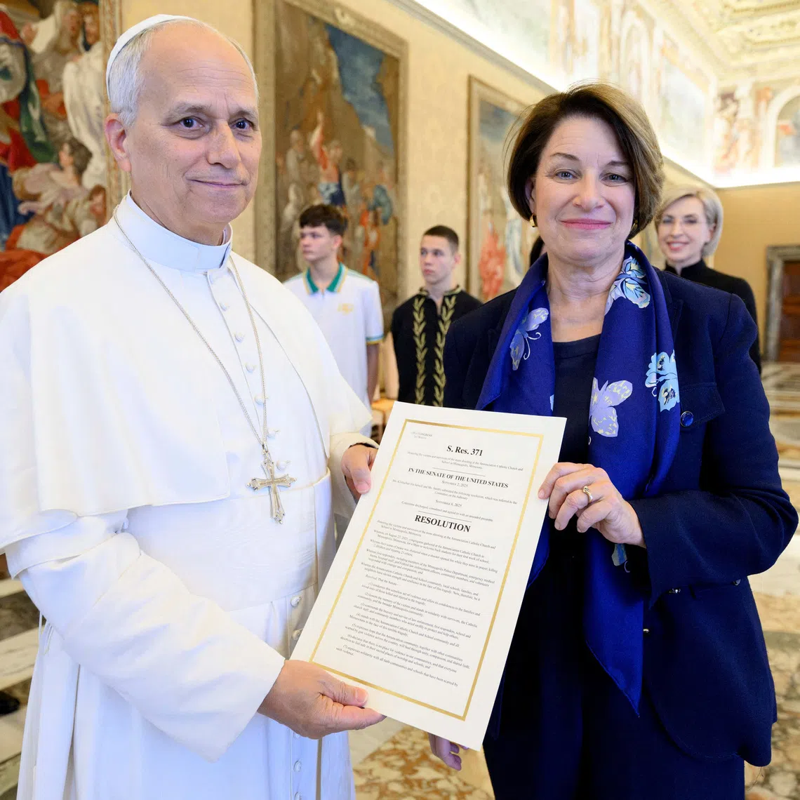 Pope Leo XIV and U.S. Senator Amy Klobuchar (D-MN) pose for a photo with a copy of a U.S. Senate bill commemorating the victims of the shooting at a Minnesota Catholic church and school, at the Vatican, November 21, 2025. Simone Risoluti/Vatican Media/­Handout via REUTERS