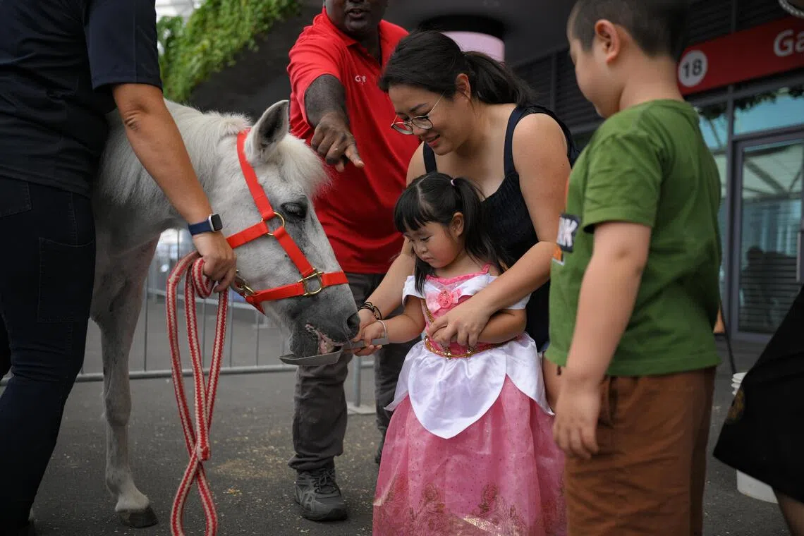 Cindy Yeo, 36, and her daughter Daenery Li, three, feeding a pony at the Gallop Stable booth.