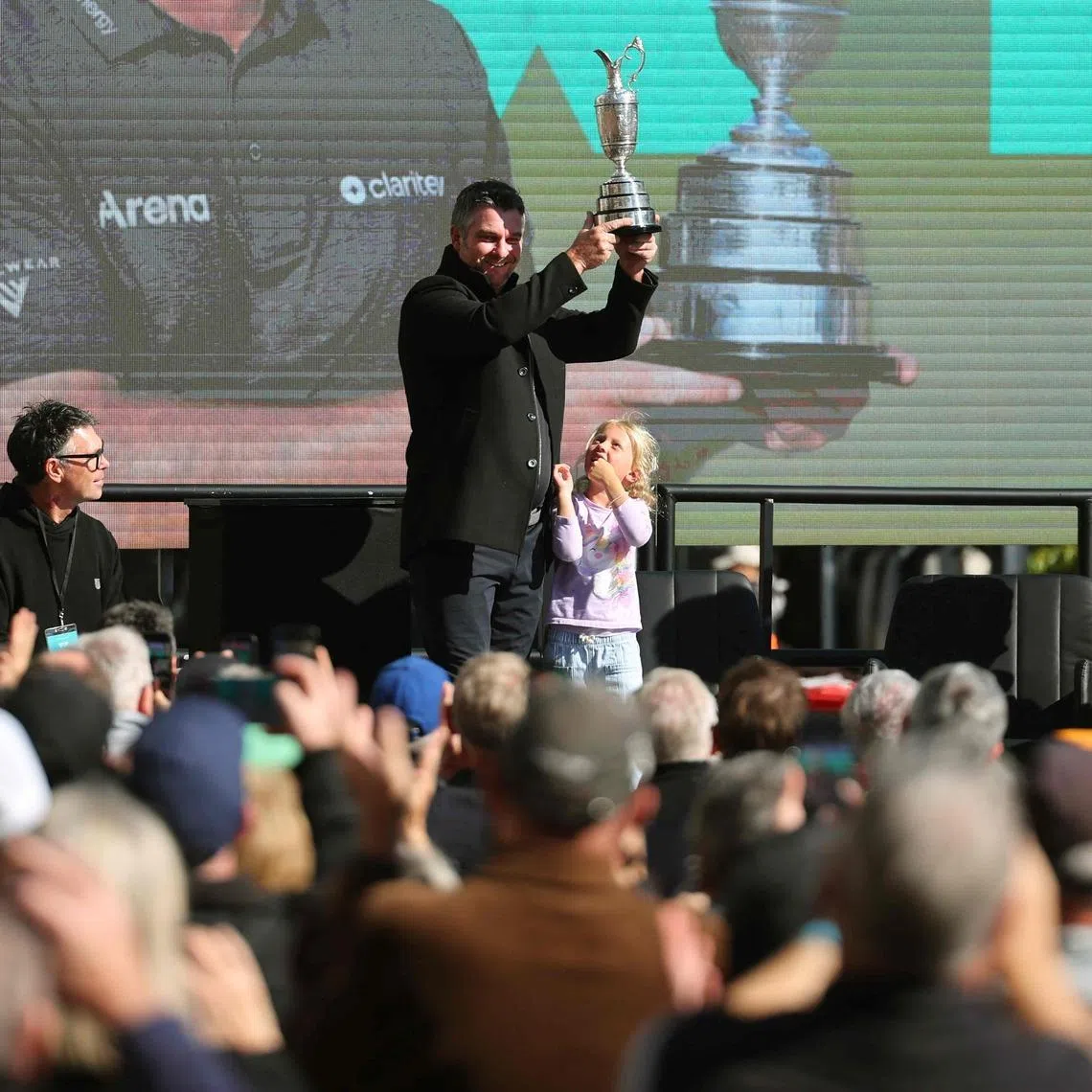 New Zealand golfer Ryan Fox holding up the Claret Jug trophy as his daughter Isobel looks up at him at a celebration in Auckland on July 28.