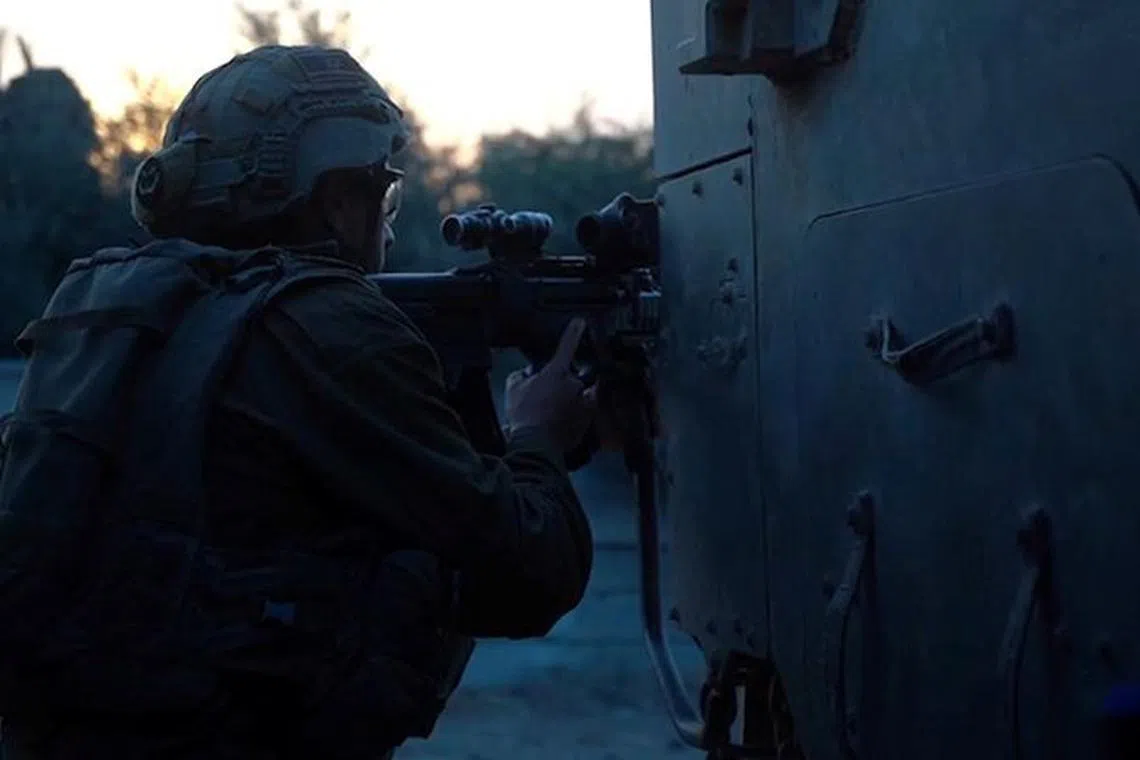An Israeli soldier holds a weapon from behind a military vehicle in a location given as Gaza, as the conflict between Israel and the Palestinian Islamist group Hamas continues, in this screengrab obtained from a handout video released on October 30, 2023.  Israeli Defence Forces/Handout via REUTERS