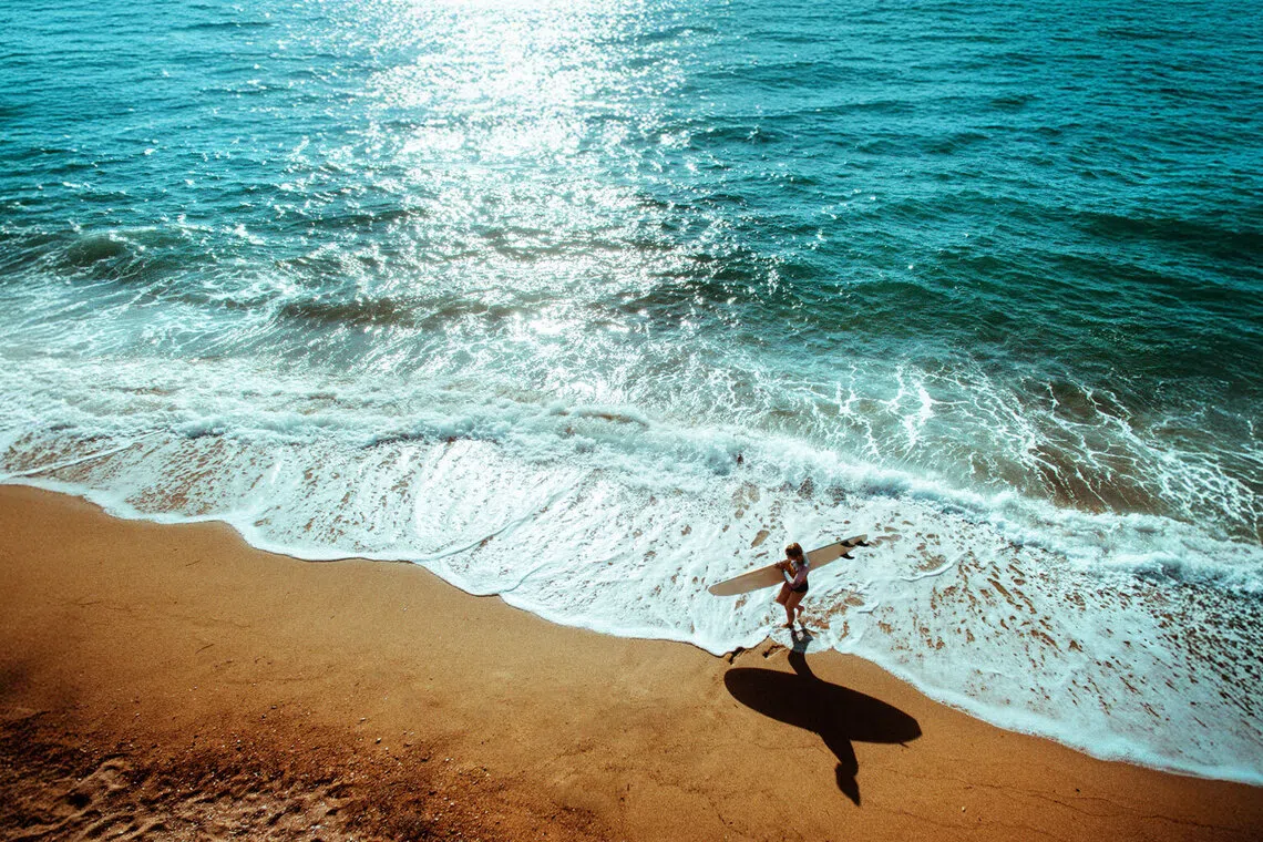 Person walking along a beach holding a surfing board