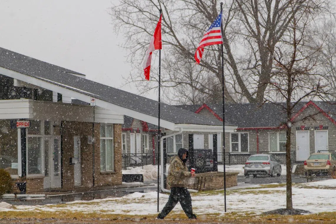 A person walks during a snow fall as a Canadian and a U.S. flag wave in the wind in Niagara Falls, Ontario, Canada, January 31, 2025. REUTERS/Carlos Osorio