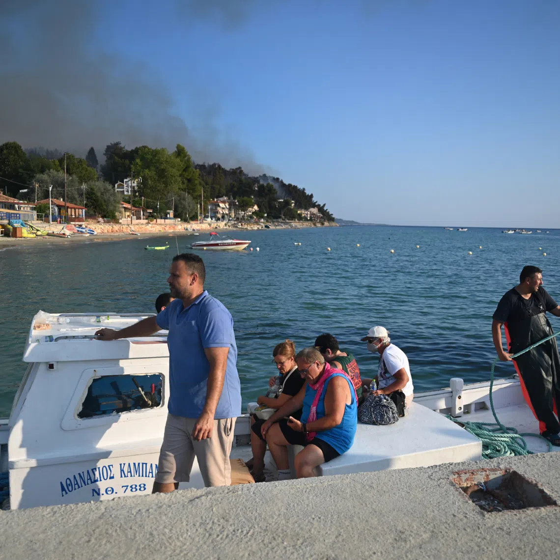 Residents and holidaymakers are transported by boats during a wildfire in Siviri, Halkidiki, Northern Greece, on Aug 13.