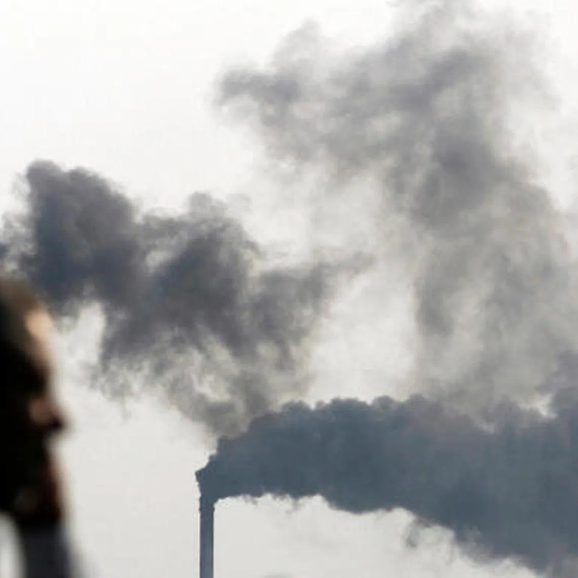A man passes in front of smoke-emitting chimneys at an industrial area of the western Indian city of Surat.