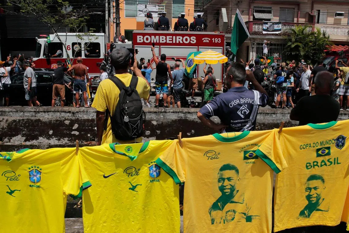 T-shirts remembering the late Brazilian football star Pele hang on a street as a firetruck transports Pele's casket to the Santos' Memorial Cemetery in Santos, Brazil, Jan 3, 2023.