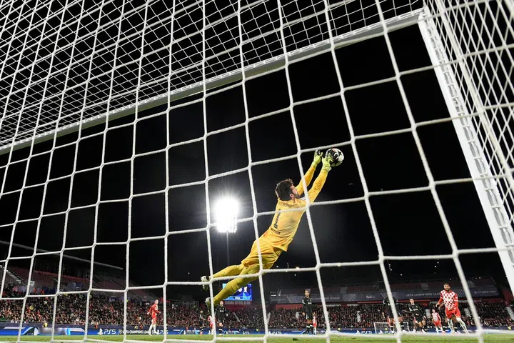 O goleiro brasileiro nº 01 do Liverpool, Alisson Becker, mergulha para salvar a bola durante a Liga dos Campeões da UEFA, partida de futebol da fase da liga entre Girona FC e Liverpool FC, no estádio Montilivi, em Girona, em 10 de dezembro de 2024. (Foto de Josep LAGO / AFP)