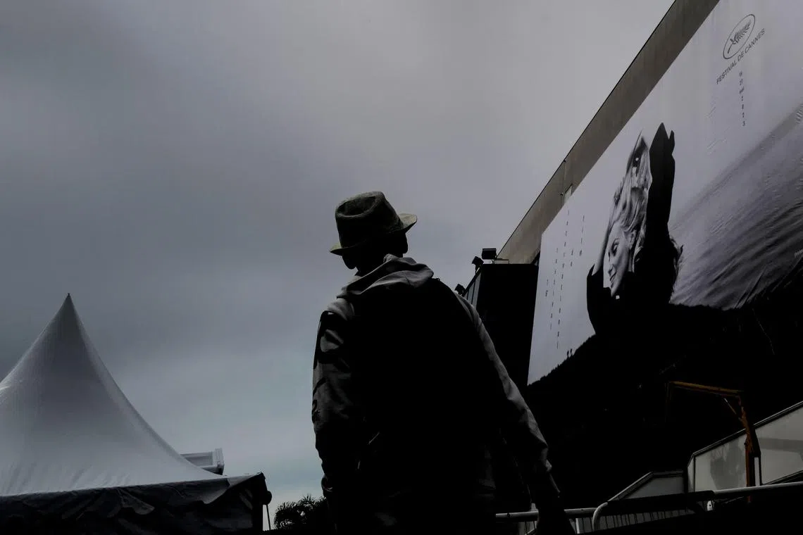 People walking in past the official poster of the 76th Cannes Film Festival featuring a photograph of actress Catherine Deneuve by Jack Garofalo, on the facade of the Palais des Festivals in Cannes, southeastern France, on May 14.