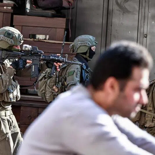 Israeli soldiers walking past a man during a military operation in the town of Qalqiya, in the occupied West Bank on Dec 4.