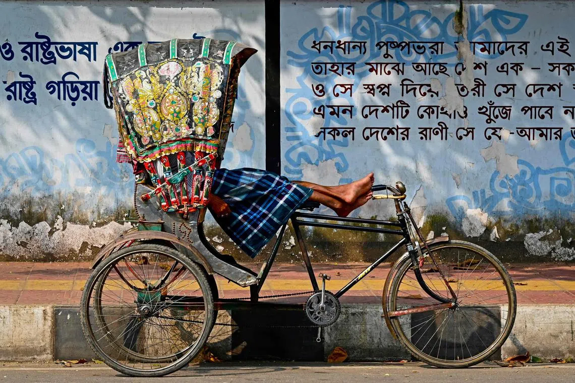 This photograph taken on Dec 13, 2023 shows a bicycle rickshaw driver resting in his vehicle by a street kerb in Dhaka. 