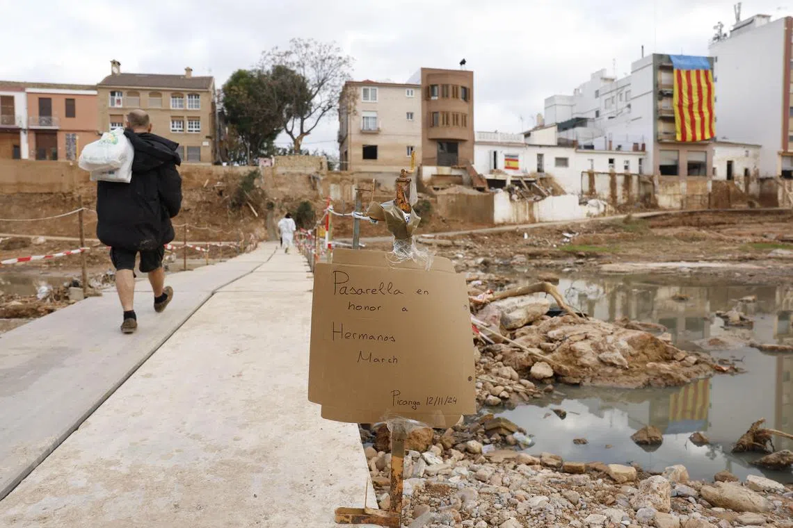 epa11737790 Several residents walk over a footbridge with a banner reading 'Footbridge in honor to March Brothers' in the Municipality of Picanya, Valencia, eastern Spain, 24 November 2024. Floods triggered by the DANA (high-altitude isolated depression) weather phenomenon hit the east of the country on 29 October 2024, devastating Valencia and neighboring provinces and leaving at least 229 people dead.   EPA-EFE/VILLAR LOPEZ