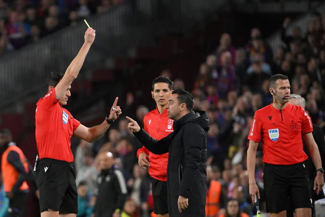 Spanish referee Juan Martinez Munuera (left) shows a yellow card next to Barcelona's Spanish coach Xavi.
