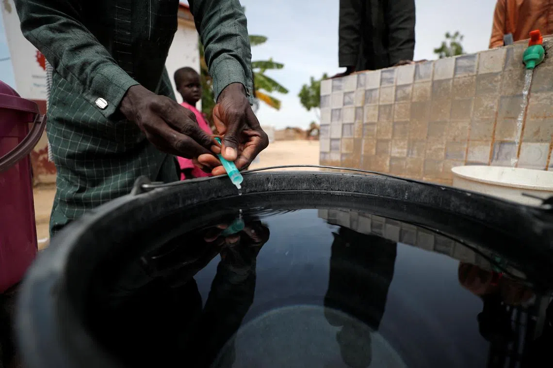 FILE PHOTO: A community health worker adds chlorine to water while internally displaced people gather to fill their buckets at the water point in Muna Garage IDP camp in Maiduguri, Borno State, Nigeria October 23, 2022. REUTERS/Christophe Van Der Perre/File Photo