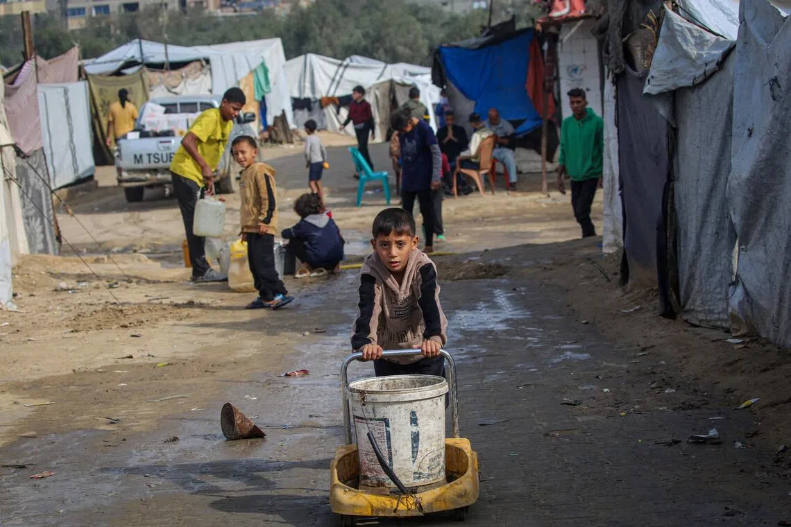 A boy pushes a bucket as children fill their containers with water at the Nuseirat camp for displaced Palestinians in central Gaza.
