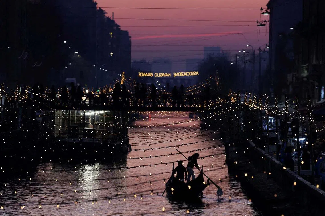 Two people rowing a gondola in the Naviglio Grande canal that was decorated with Christmas lights, in Milan, Italy, Dec 20, 2023. 