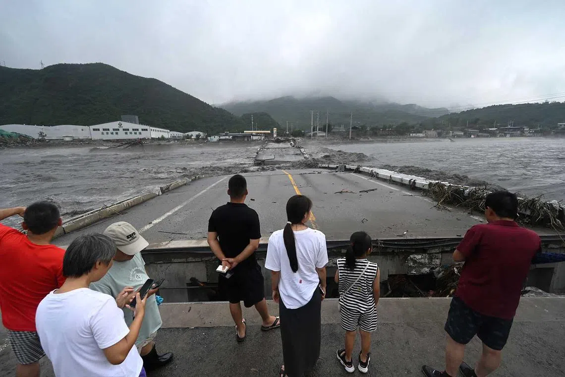 People watch a collapsed bridge on the Dashihe River after heavy rains in Fangshan district in Beijing on Aug 1, 2023.
