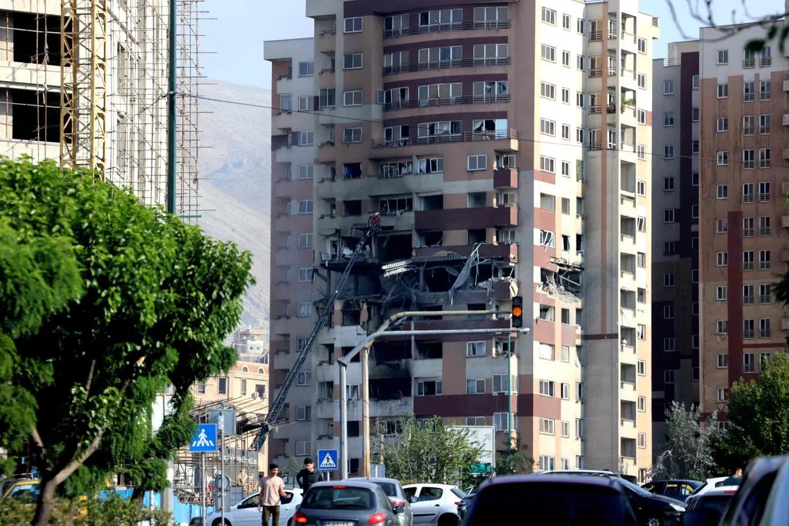 People walk past traffic in front of a building targeted by an Israeli strike in the Iranian capital Tehran on June 13, 2025.