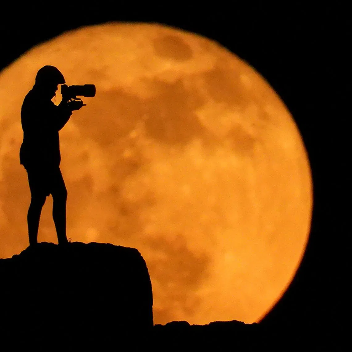 A photographer is silhouetted against the full moon known as the strawberry moon in Arinaga, on the island of Gran Canaria, Spain, June 11, 2025. REUTERS/Borja Suarez      TPX IMAGES OF THE DAY     