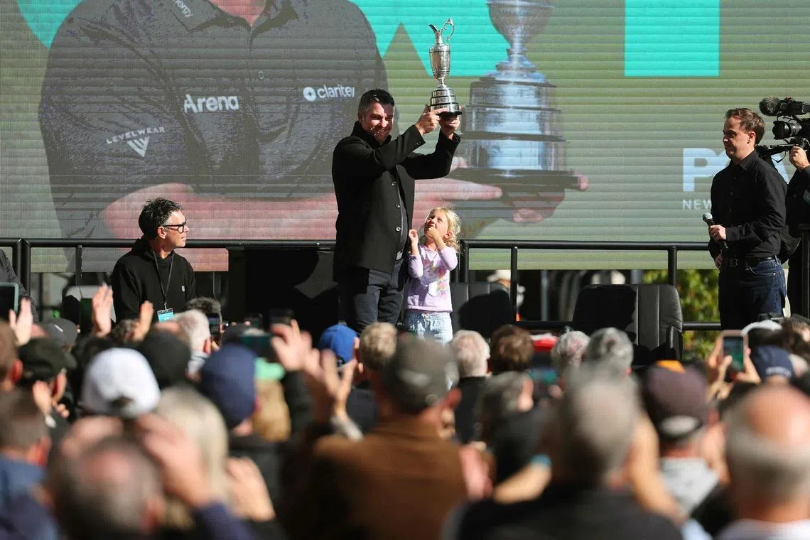 New Zealand golfer Ryan Fox holding up the Claret Jug trophy as his daughter Isobel looks up at him at a celebration in Auckland on July 28.