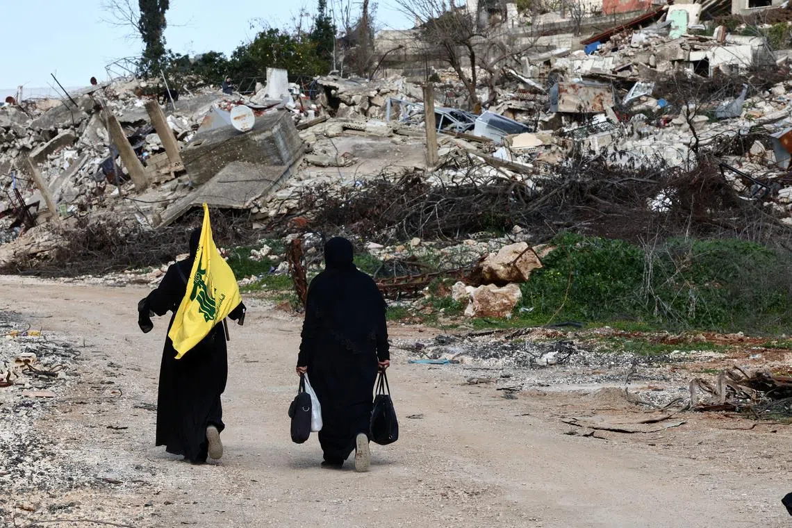 FILE PHOTO: Women walk near destroyed buildings, with one holding the flag of Hezbollah, in the southern Lebanese village of Kfar Kila, after an Israeli military spokesperson said that Israel would keep troops in several posts in southern Lebanon past the deadline for them to withdraw, February 18, 2025. REUTERS/Emilie Madi/File Photo