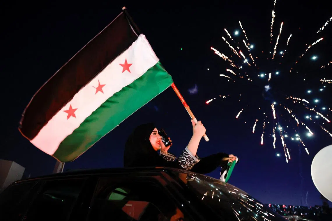 A woman holds up the flag adopted by the new Syrian rulers, as people celebrate after fighters of the ruling Syrian body ousted Syria's Bashar al-Assad, in the Damascus old city, Syria, December 13, 2024. REUTERS/Ammar Awad