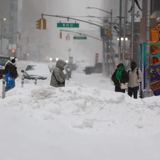 People cross Sixth Avenue in the snow in New York on Jan 25, 2026.