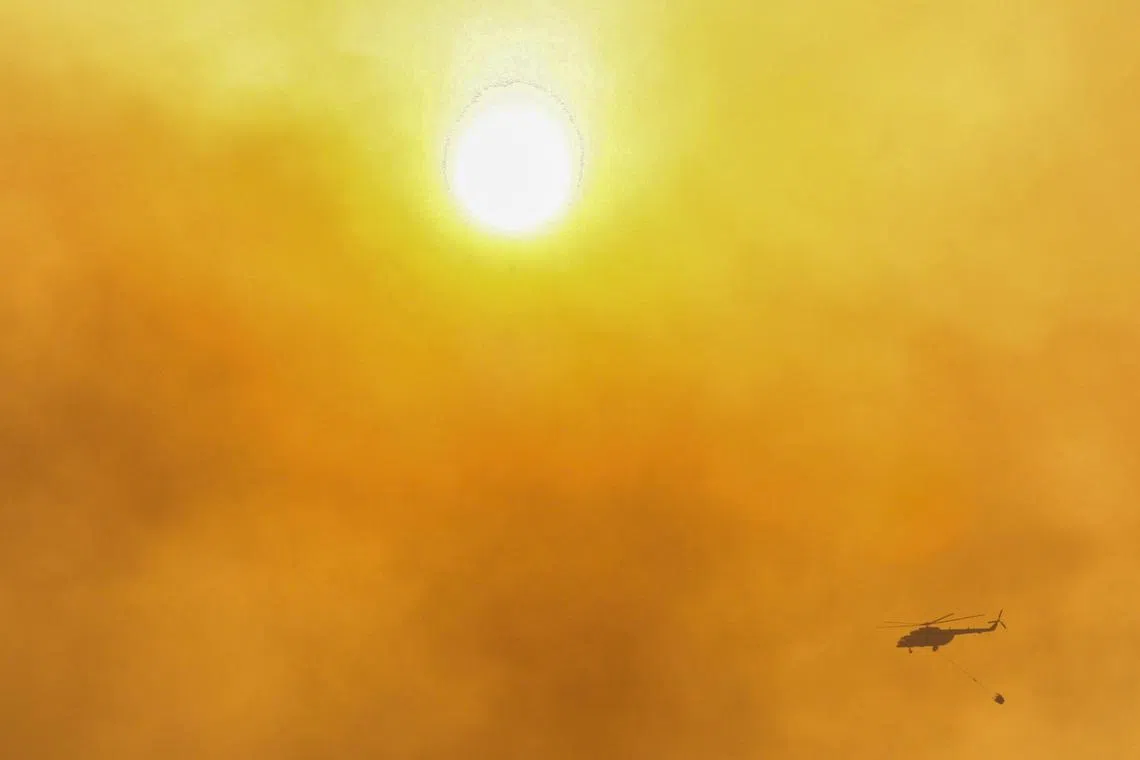 A firefighting helicopter flies through the smoke that raises from wildfires during a sunset near Marmaris, a town in Mugla province, Turkey, June 23, 2022. REUTERS/Kenan Gurbuz/File Photo