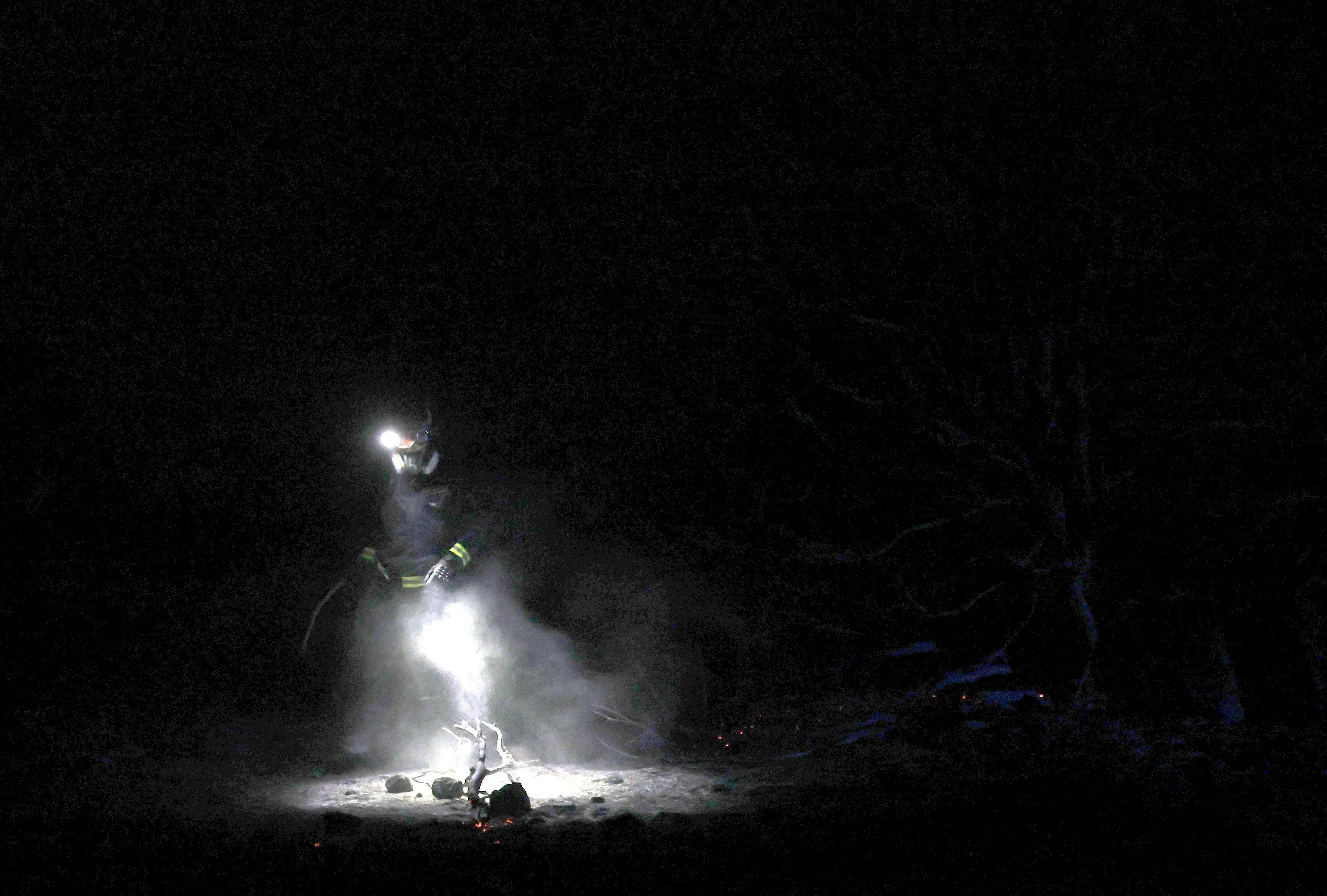 TOPSHOT - A firefighter walks in the night amid a wildfire in Fresnedillas area, near El Escorial, 60 kms northwest of Madrid, early on July 25, 2026. Spanish firefighters hoped to get control of wildfires raging near Madrid on Saturday but an official warned that erratic winds threatened to fan the blazes further. The worst wildfires in the Madrid region's history rage west of the Spanish capital, forcing authorities to evacuate or order around 60,000 people to remain indoors. (Photo by Oscar DEL POZO / AFP)