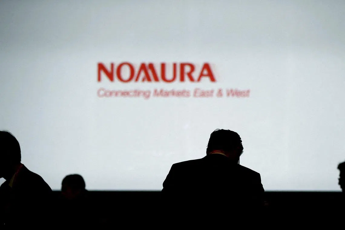 Investors stand in front of a screen showing the logo of Nomura Holdings in Tokyo, Japan.