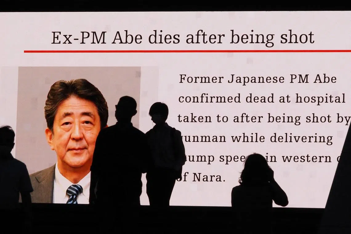 Pedestrians are silhouetted against a large screen showing an image of former Japanese prime minister Shinzo Abe in the Akihabara district of Tokyo on July 8, 2022.