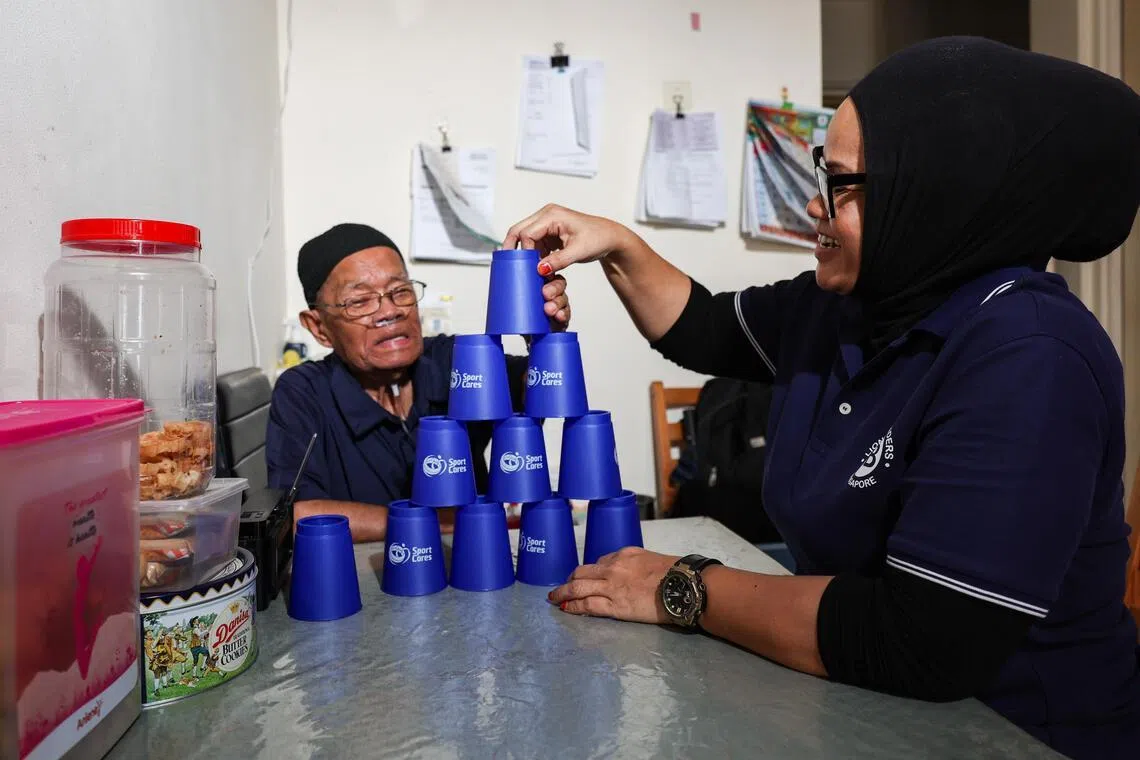 Radiana Ahmad (right), 49, a healthcare assistant, guiding Abu Alias Man (left), 89, through a cup-stacking exercise during a home visit in Clementi on June 29, 2026. ST PHOTO: BRIAN TEO