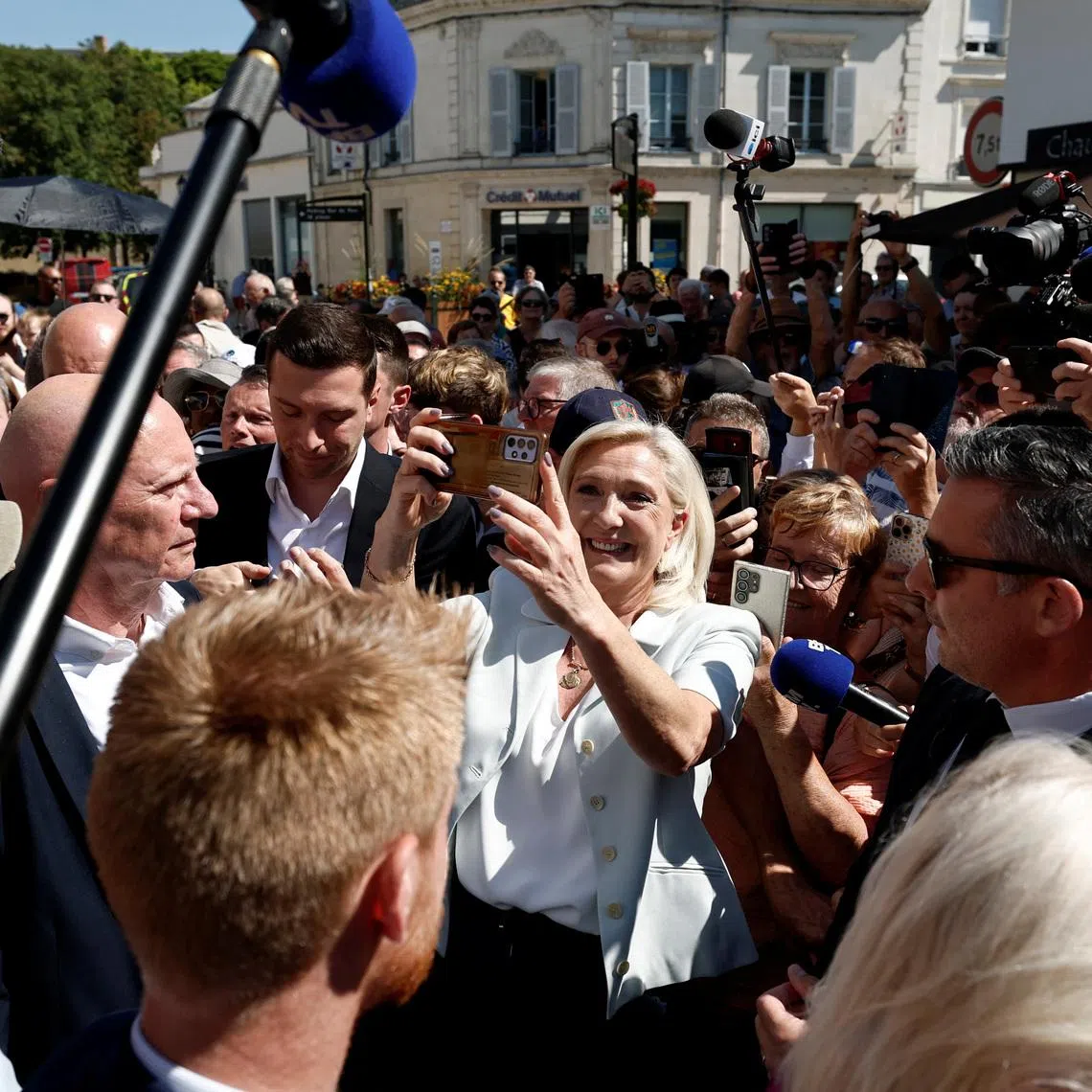 French far-right leader Marine Le Pen makes a selfie with supporters next to Jordan Bardella, president of the French far-right Rassemblement National (National Rally - RN) political party, during a visit at a market in La Fleche, in the Sarthe department, a day after Le Pen announced her candidacy for the 2027 French presidential election following an appeals court ruling that shortened her ban on running for office while upholding her conviction for embezzling EU funds, France, July 8, 2026. REUTERS/Benoit Tessier