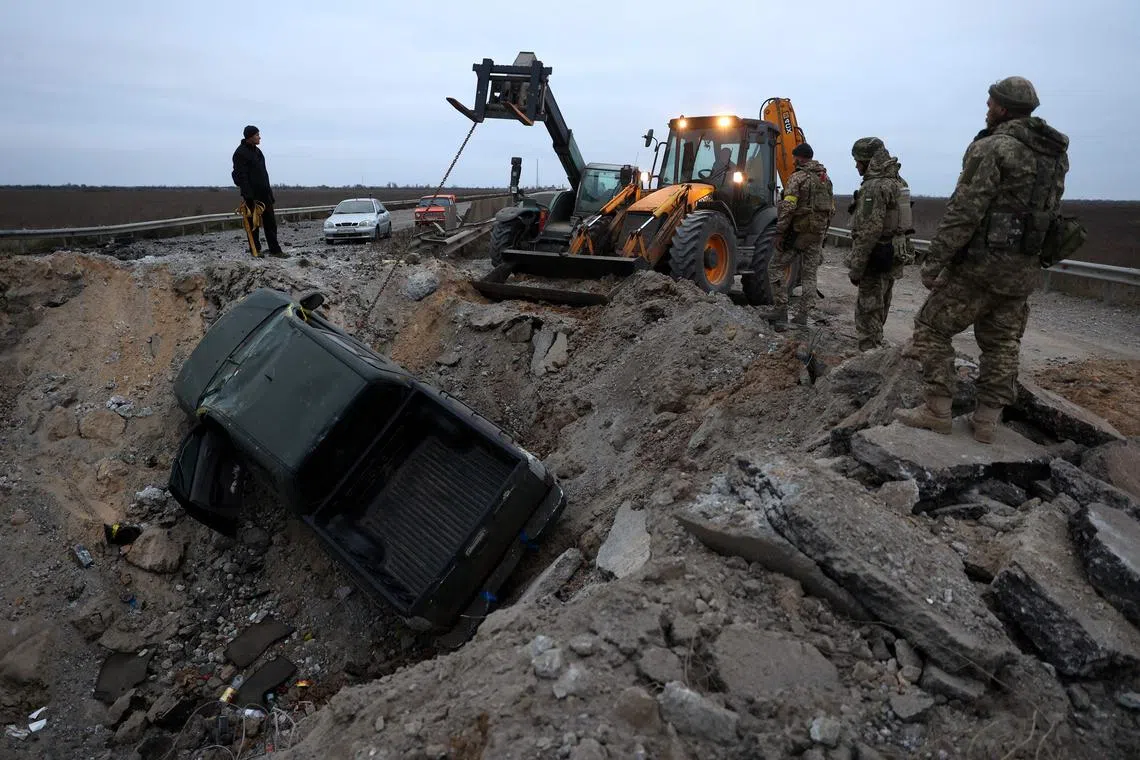 Ukrainian soldiers pull a car out of a crater on the road in Kherson region on Nov 13, 2022.