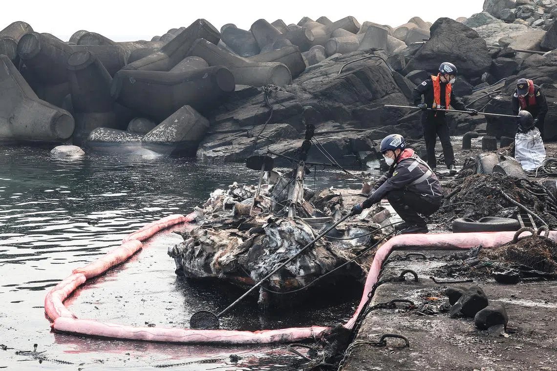 Maritime police officers cleaning up oil leaked from a burnt-out fishing boat at a port in Yeongdeok, South Korea, on March 26, 2025.