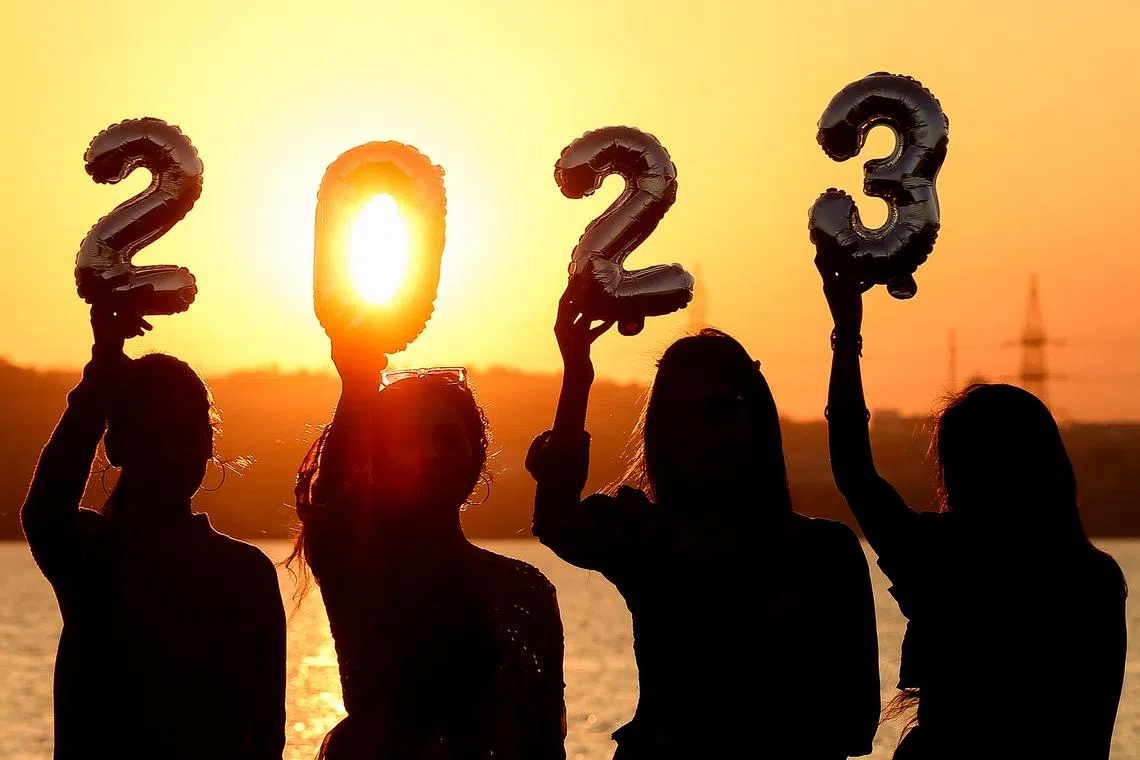 Women are silhouetted against the setting sun as they hold up numeric shaped balloons on the eve of New Year on Dec 31, 2022. 