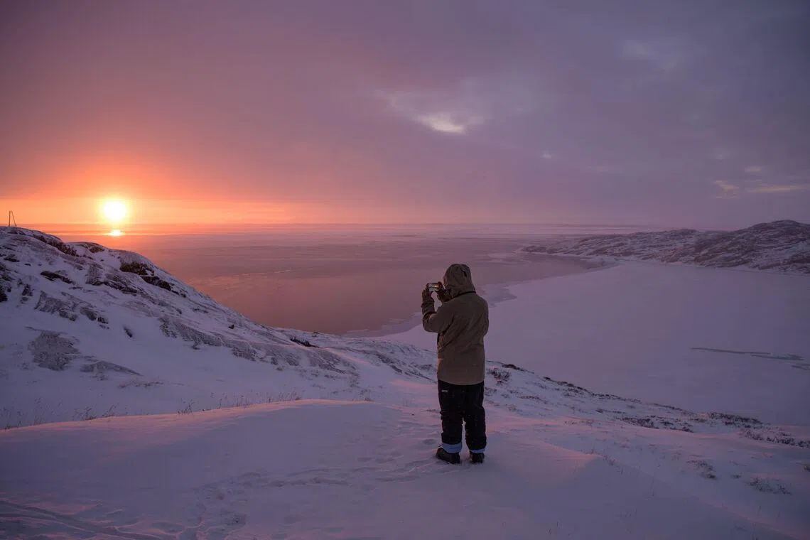 TOPSHOT - A boy takes a photo of the sunset, with the icy bay in the background, in Ilulissat, Greenland, on March 16, 2026. (Photo by Florent VERGNES / AFP)
