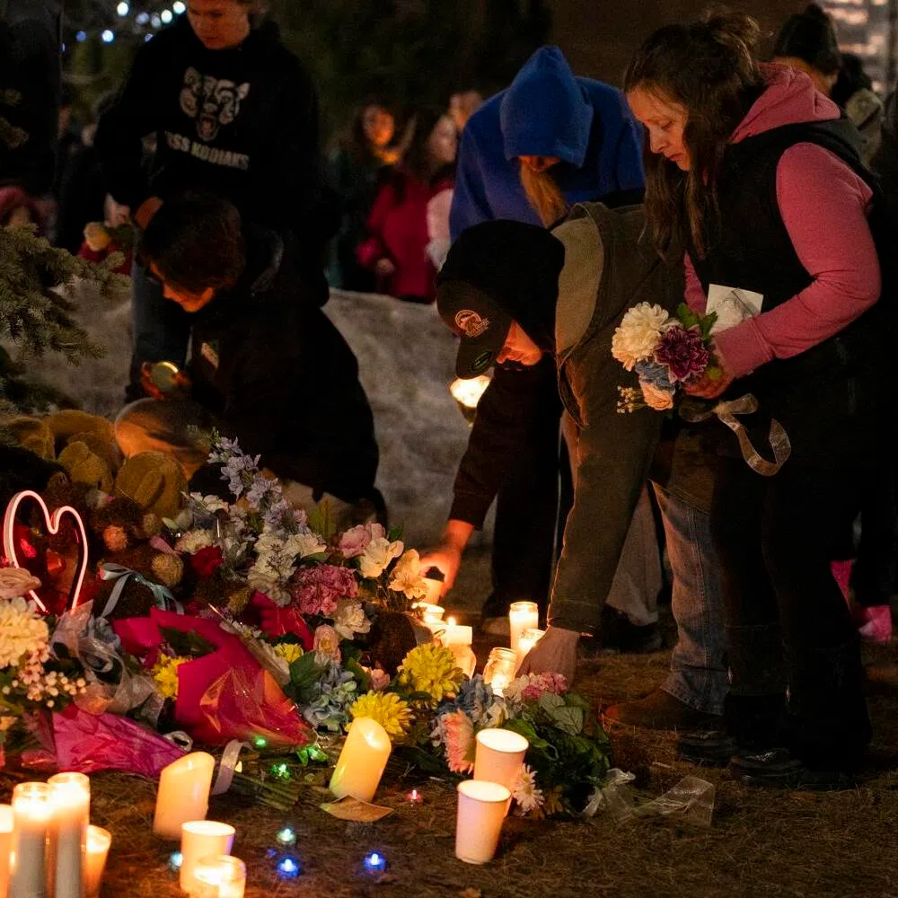 Community members place flowers at a memorial during a candlelight vigil for the victims of Tumbler Ridge Secondary School where a mass shooting took place a day earlier, in the small town of Tumbler Ridge, British Columbia, on February 11, 2026. Canadian police said February 11 an 18-year-old carried out a mass shooting in a remote mining town, killing six people at a local school, after slaying her mother and stepbrother. Police commander Dwayne McDonald said authorities still don't know the motive in Tuesday's mass shooting in Tumbler Ridge, but the shooter, who took her own life, was known to have mental health issues. (Photo by Paige Taylor White / AFP)